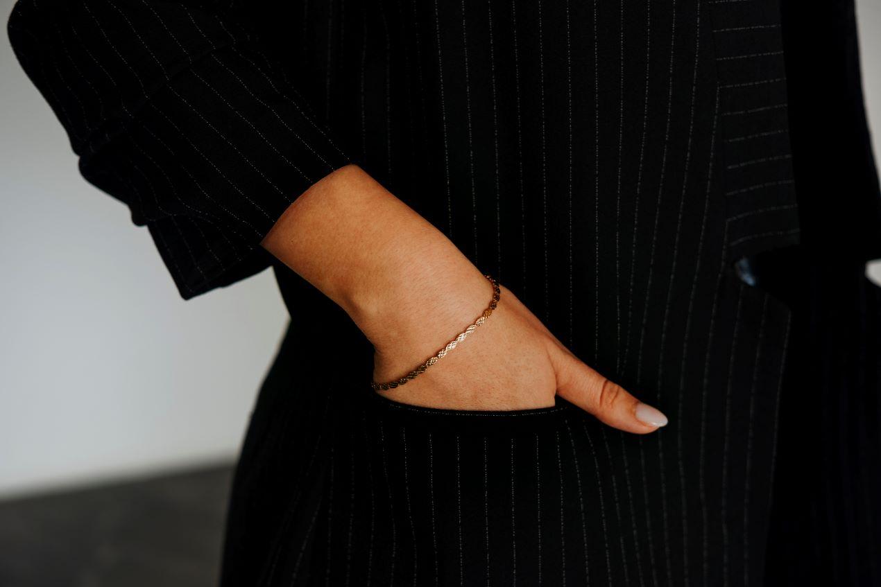 Goldenes Armband an einer Frau im schwarzen Business-Outfit, stilvoll kombiniert mit klassischem Design und dezentem Schmuck.